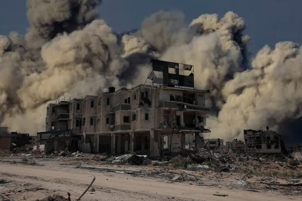 A bombed out Gaza building, explosive smoke and dust int he background