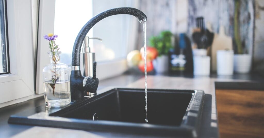 A modern kitchen sink with running water, a sleek faucet, and a vase on the countertop.